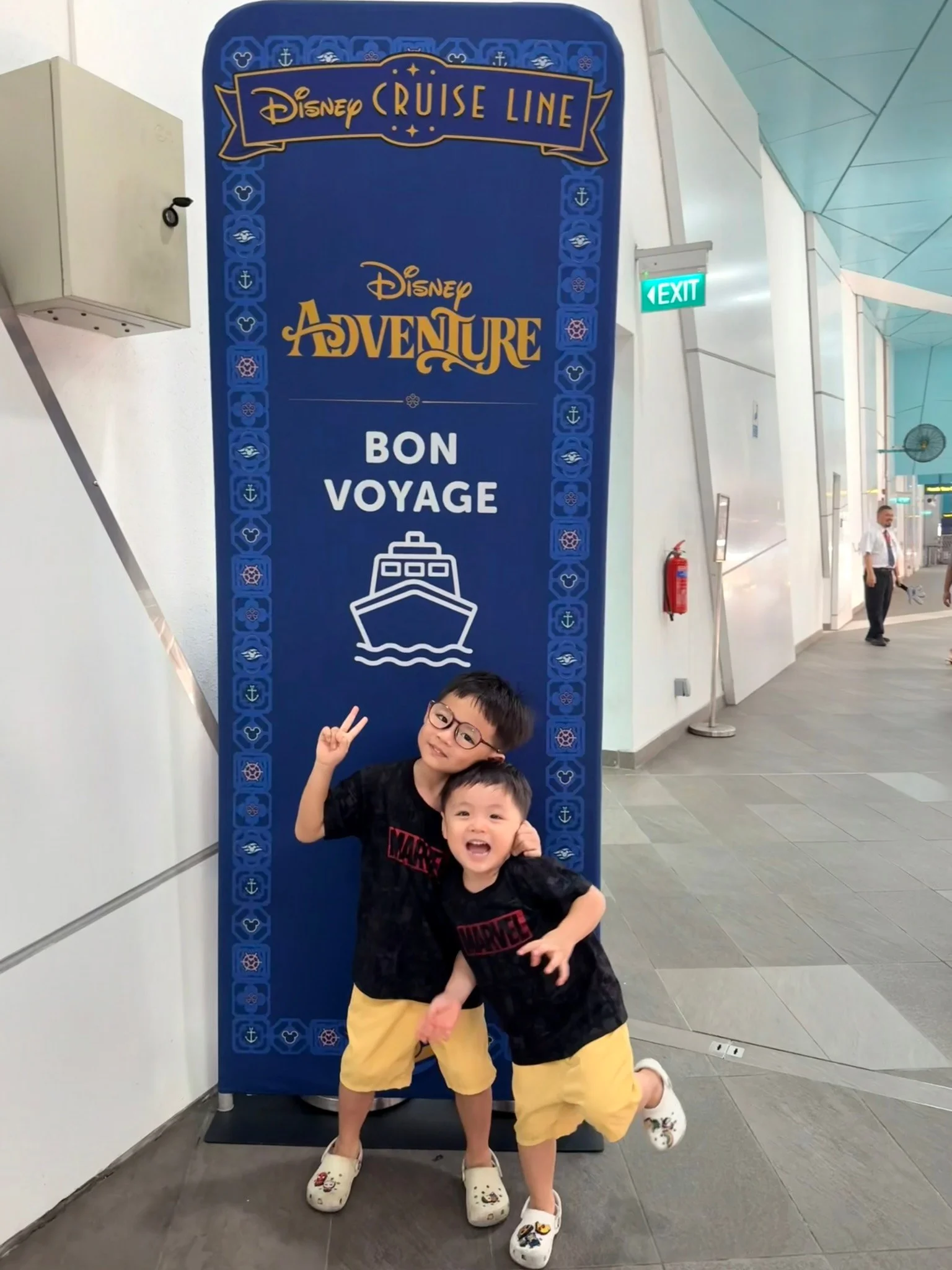 Lucas and Ethan posing in front of a Disney Adventure “Bon Voyage” sign at the cruise terminal.