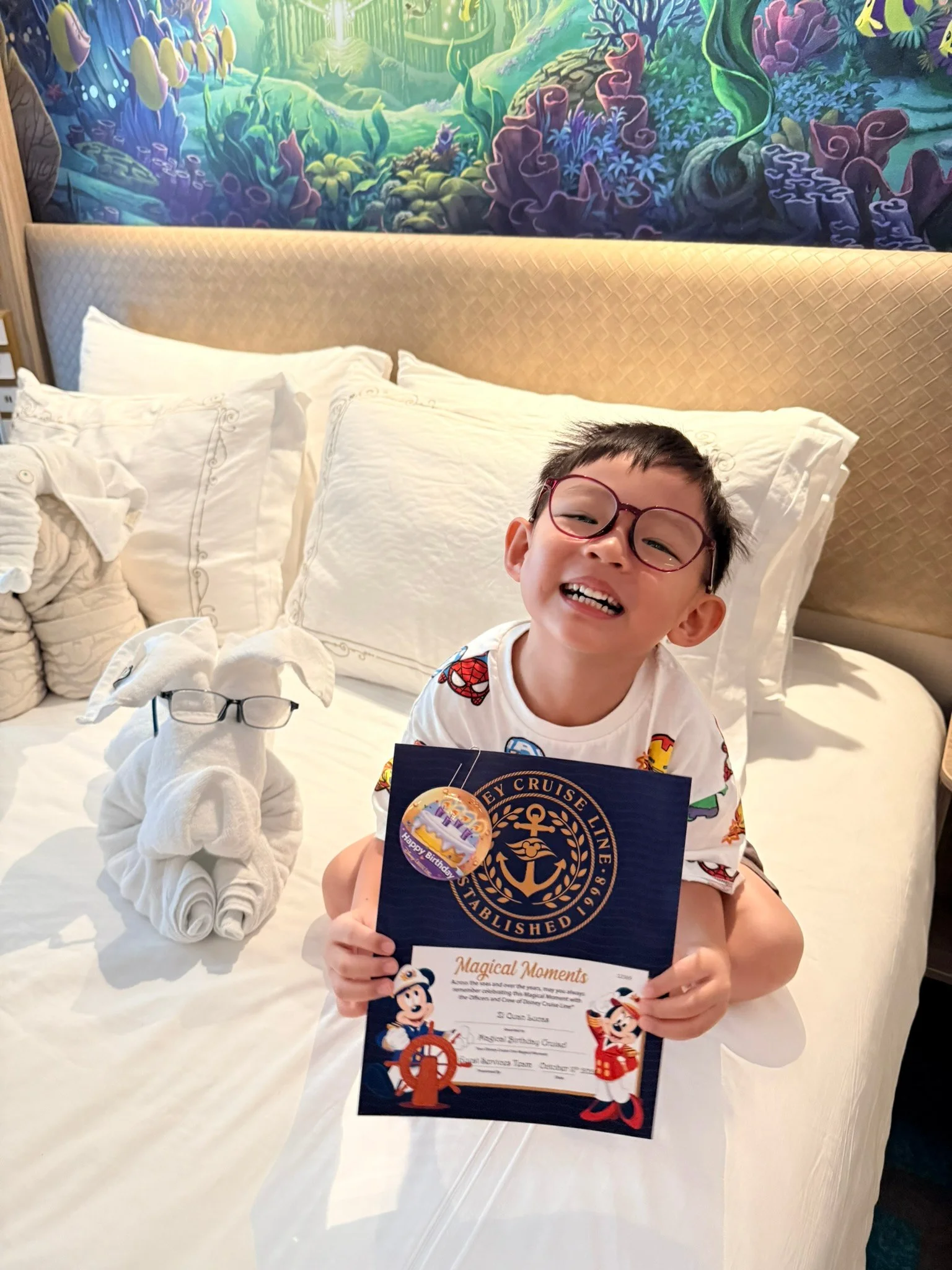 Lucas smiling on the bed with his birthday certificate.
