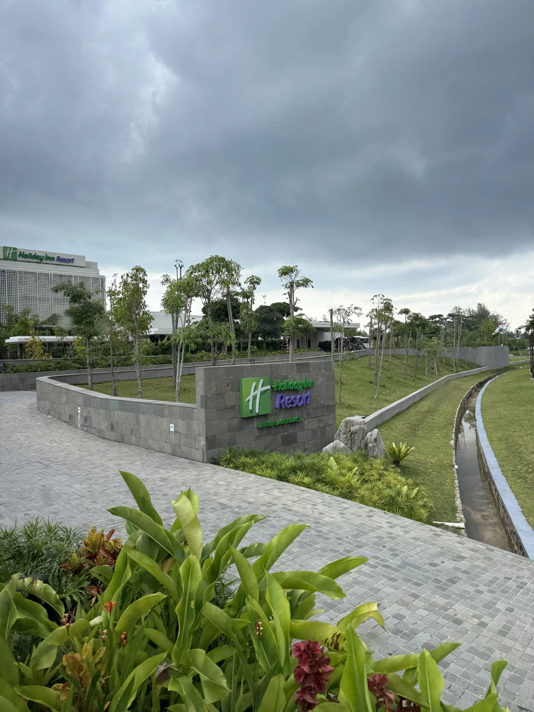 The landscaped entrance to Holiday Inn Resort Bintan Lagoi Beach beneath a cloudy sky.